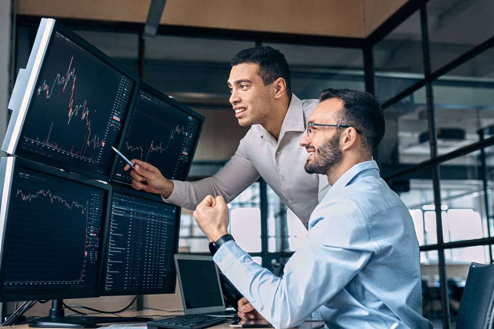 TwoMenTradersSittingAtDeskAtOfficeTogetherMonitoring | Latino Inversores - Inversión y Trading En Línea